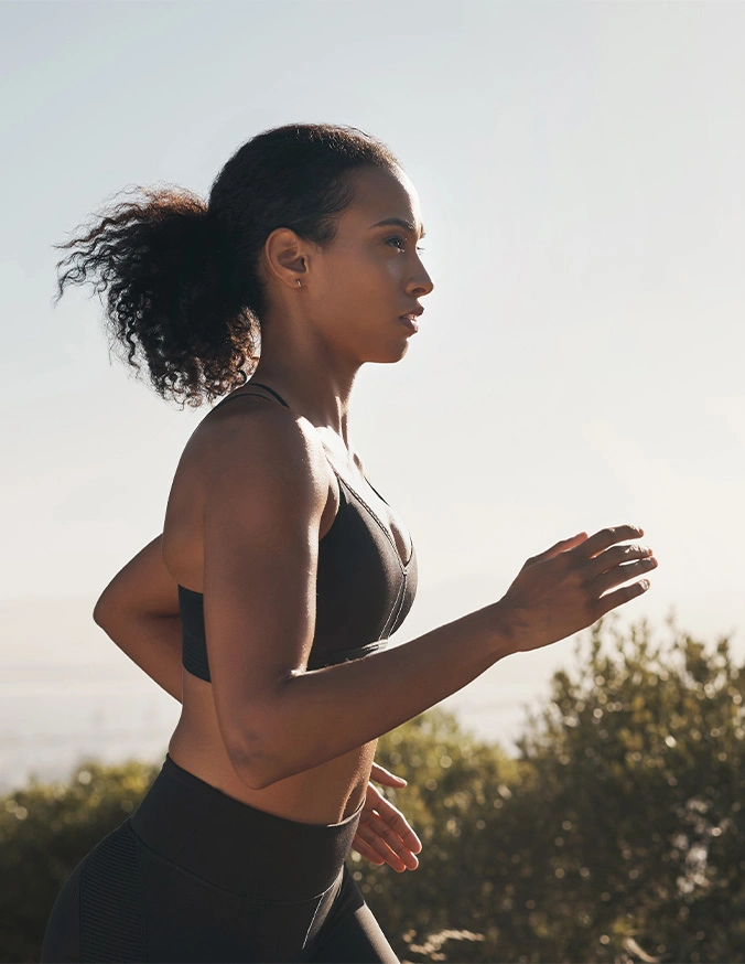 Woman running outdoors at sunset wearing athletic wear and fitness tracker on arm - Awake lipo vs fat freezing in Brookfield and Appleton, WI.