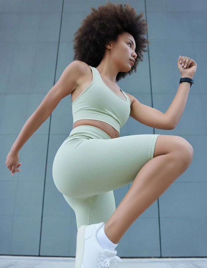 Woman in mint green athletic wear performing high knee exercise outdoors against modern wall - Legs and thighs in Brookfield and Appleton, WI.
