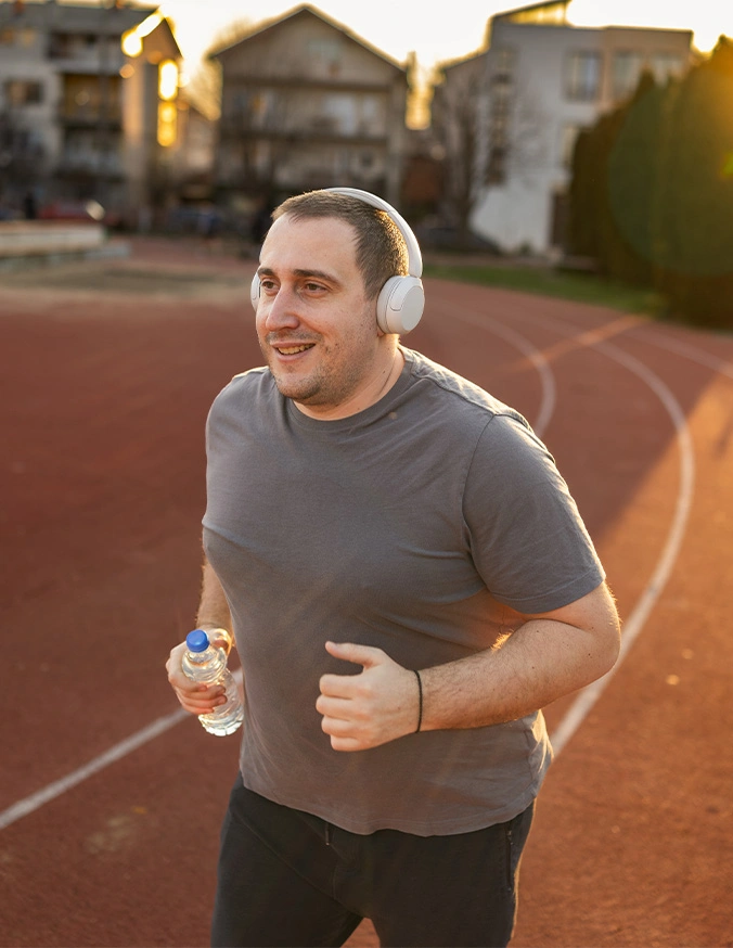 Man jogging on outdoor track wearing headphones and gray shirt during golden hour sunset - Male belly in Brookfield and Appleton, WI.
