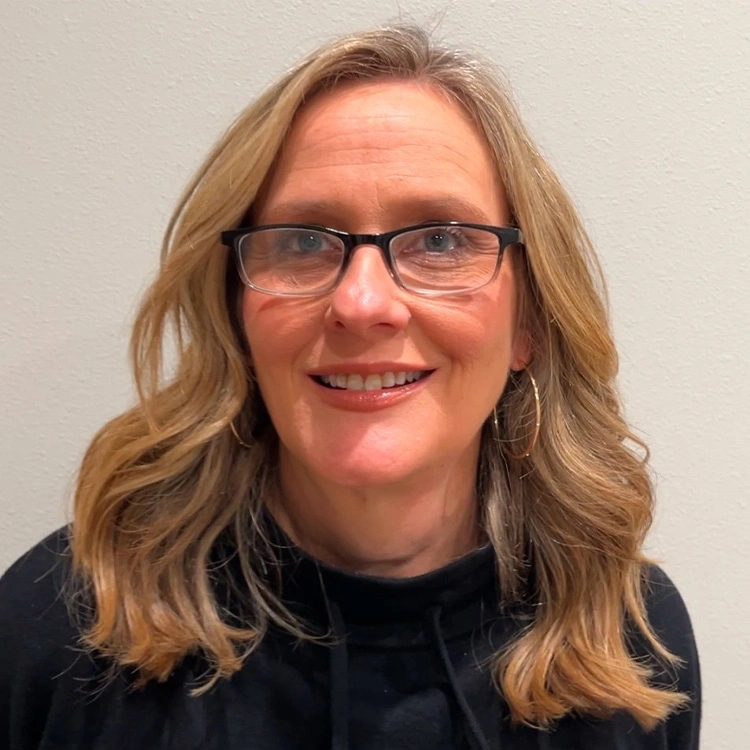 Smiling woman with blonde wavy hair and glasses wearing black top for patient stories article
