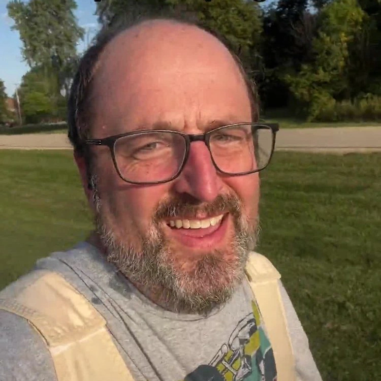 Smiling bearded man wearing glasses outdoors in park setting, patient testimonial portrait