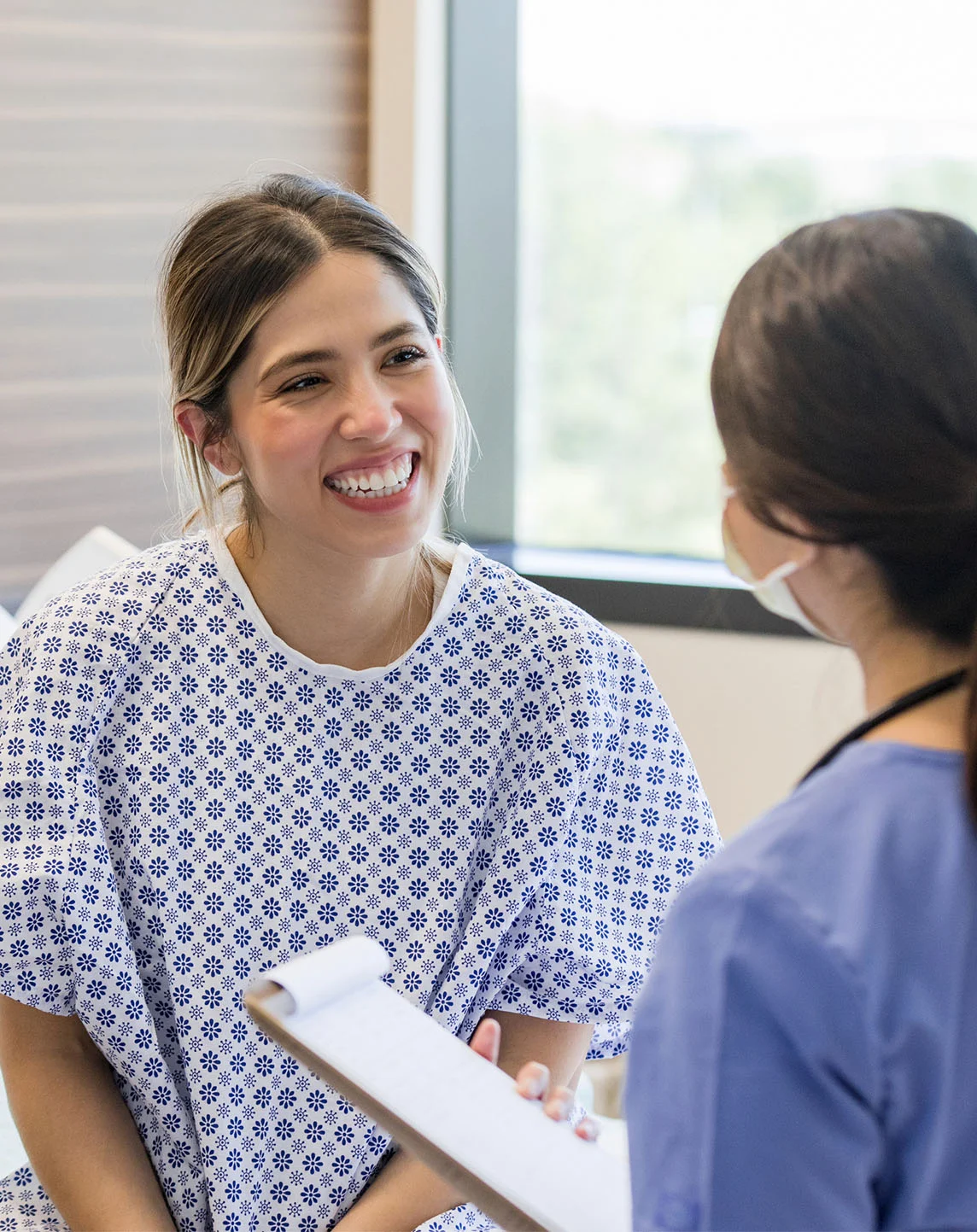 Healthcare professional consulting with smiling female patient in hospital gown during medical appointment - In Appleton, Brookfield, Milwaukee, WI & Gurnee, IL