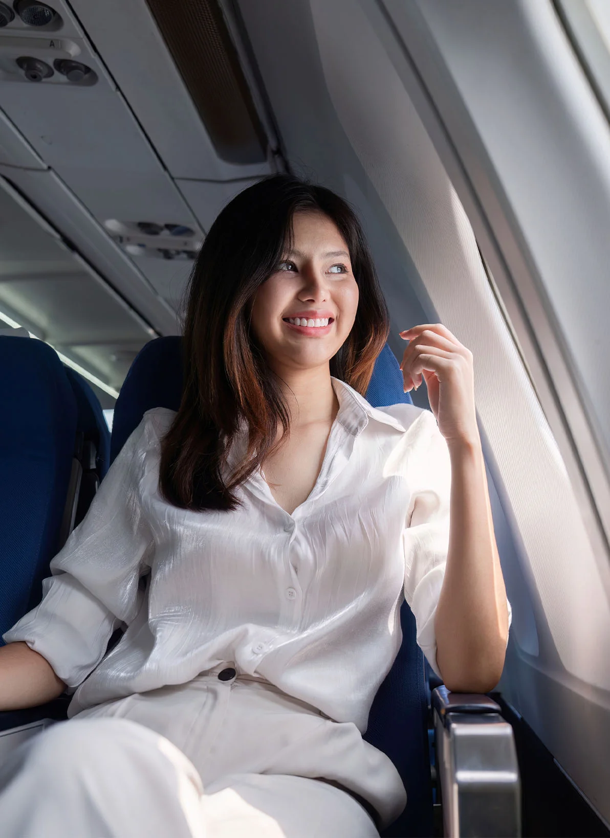 Woman smiling while sitting by airplane window in white outfit, holding passport during flight - In Appleton, Brookfield, Milwaukee, WI & Gurnee, IL