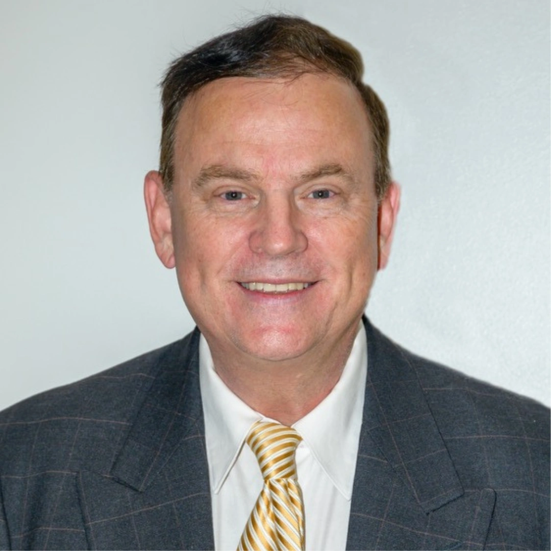 Dr. conrardy in navy suit and striped tie smiling at camera against neutral background