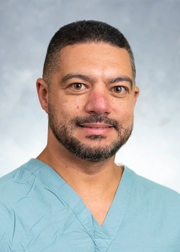 Hamdy Elhadary PA-C in blue scrubs smiling at camera against gray background