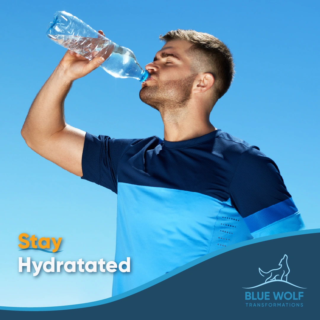 Athletic man in blue shirt drinking water from bottle against clear sky, demonstrating proper hydration during exercise