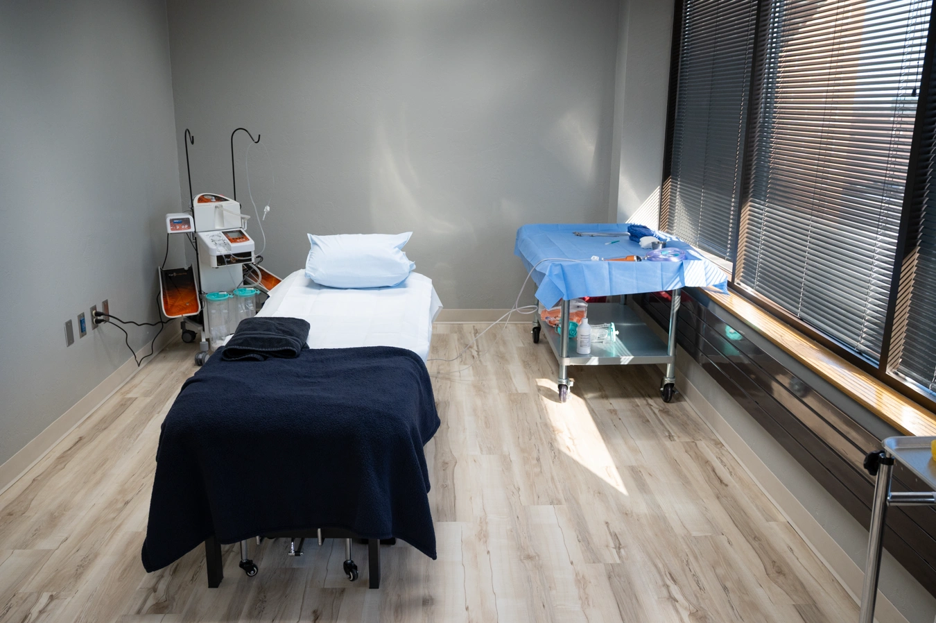 Medical treatment room with examination table, equipment cart, and window with natural light - In Appleton, Brookfield, Milwaukee, WI & Gurnee, IL