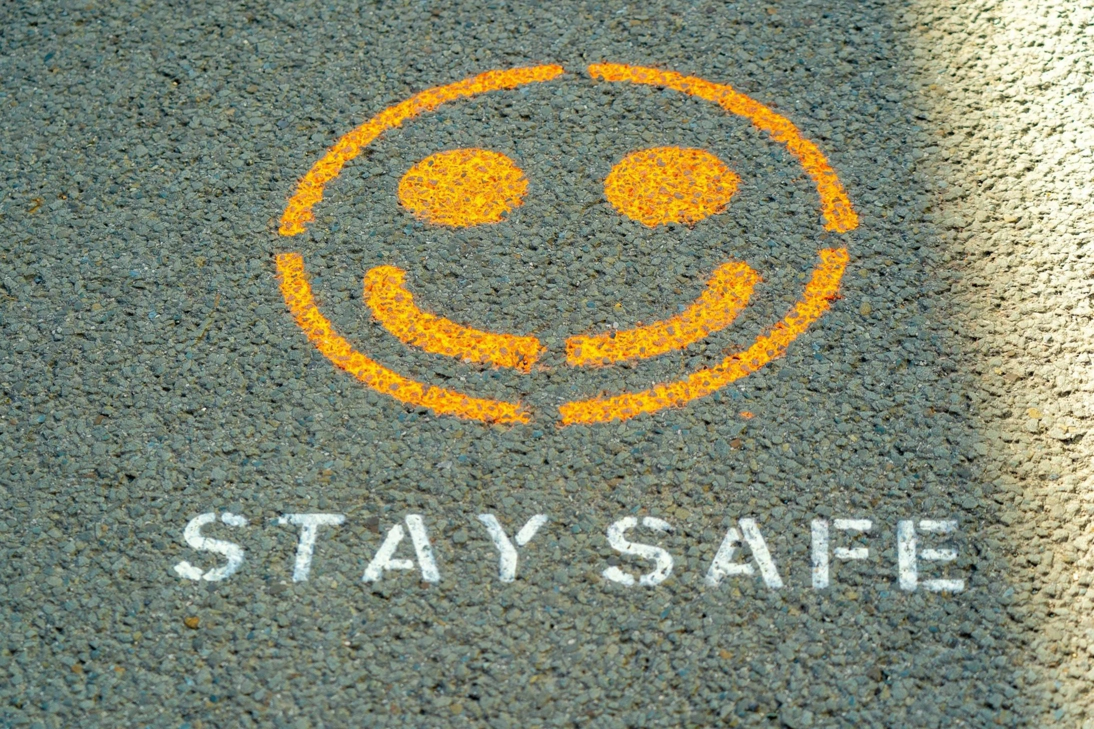 Yellow smiley face with "STAY SAFE" text painted on pavement surface for pedestrian safety during tour