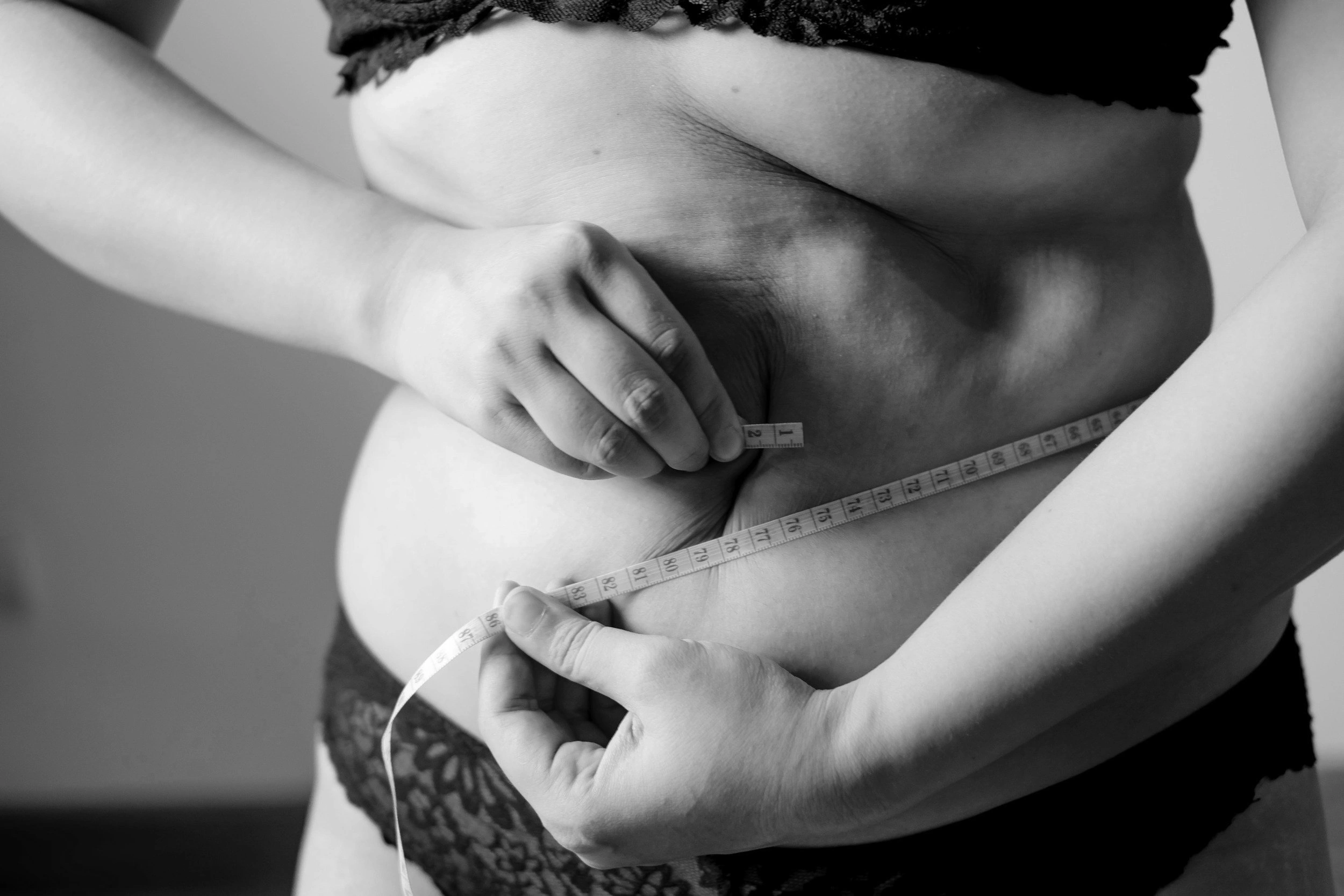 woman holding belly in black and white with measuring tape photo - In Appleton, Brookfield, Milwaukee, WI & Gurnee, IL
