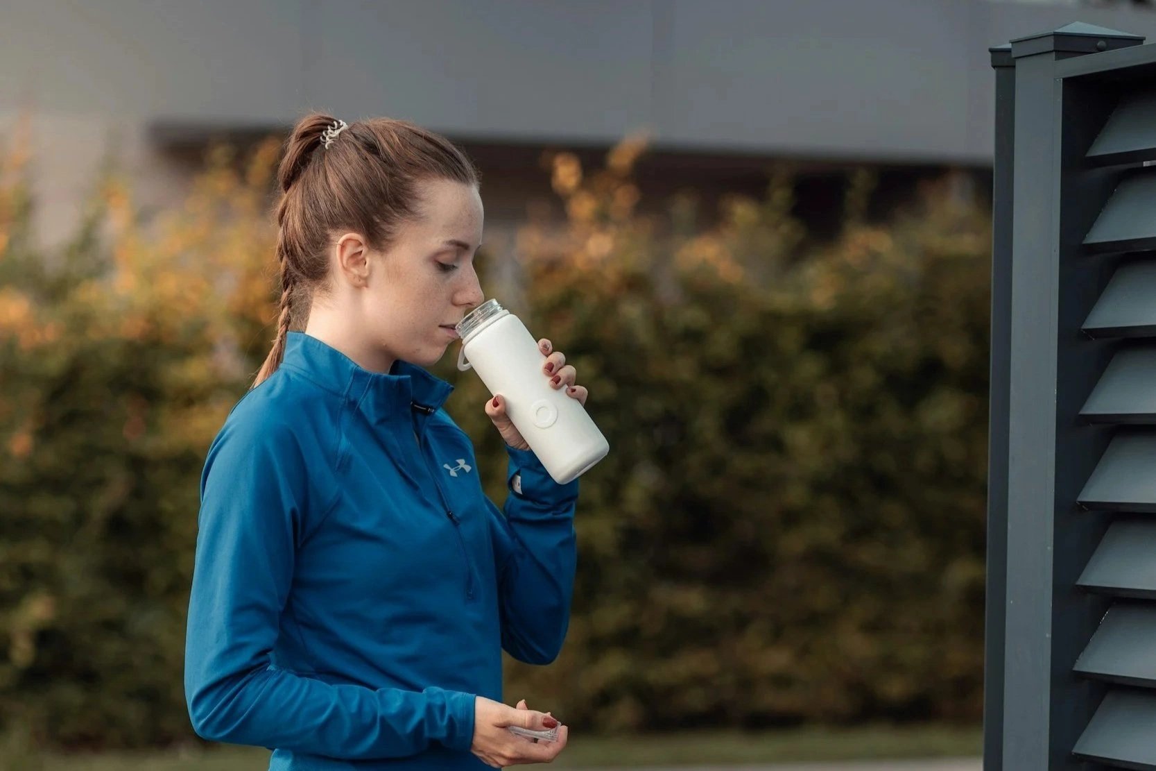 Woman in blue athletic jacket drinking from white water bottle outdoors during fitness tour - In Appleton, Brookfield, Milwaukee, WI & Gurnee, IL